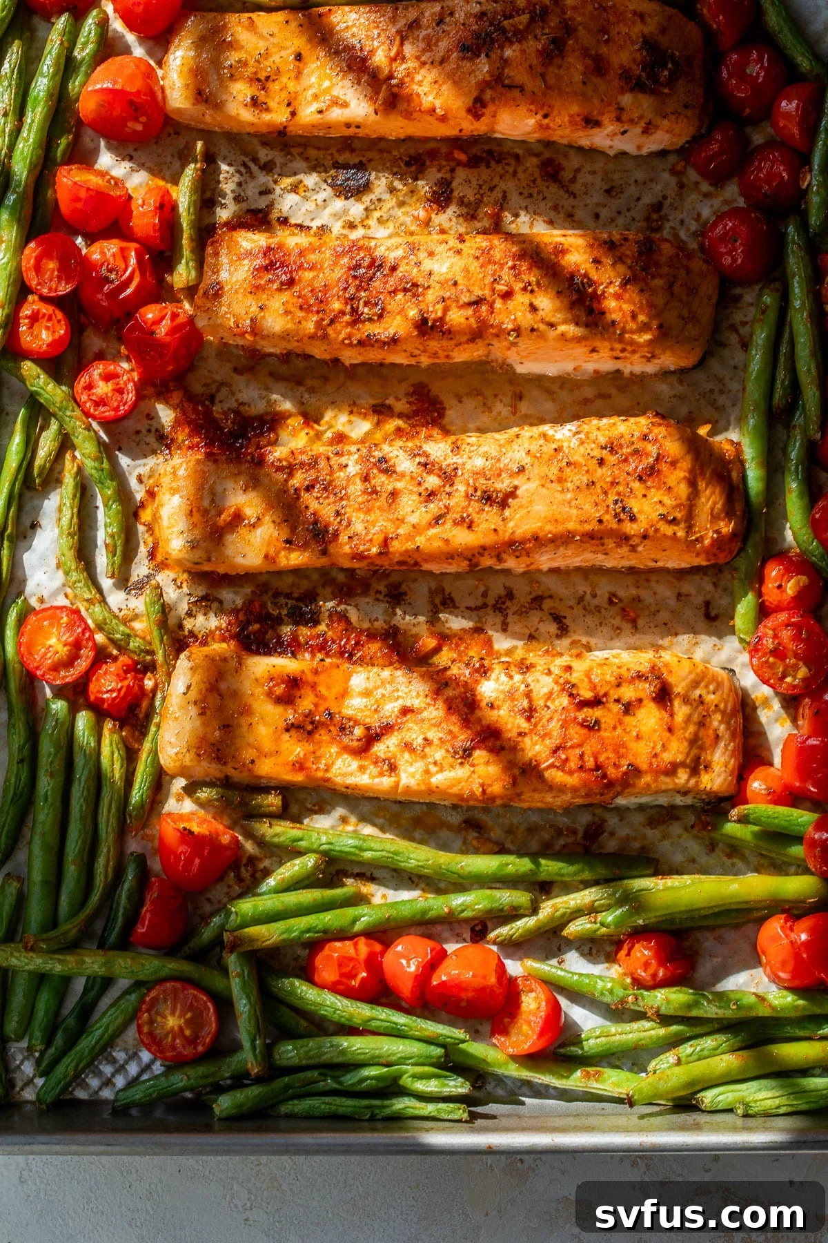overhead view of roasted salmon fillets, green beans, and tomatoes on a sheet pan.