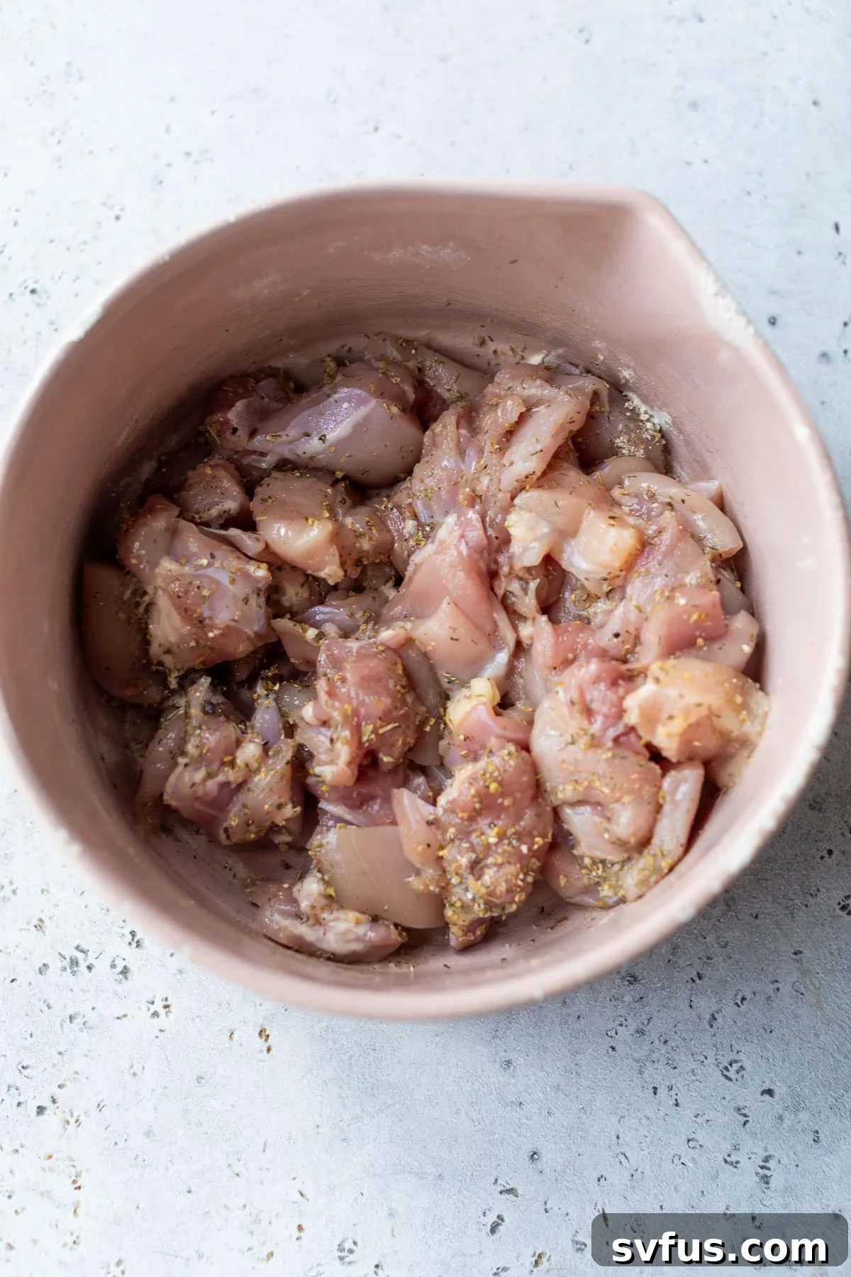 overhead view of raw chicken thigh pieces in a bowl with seasonings.