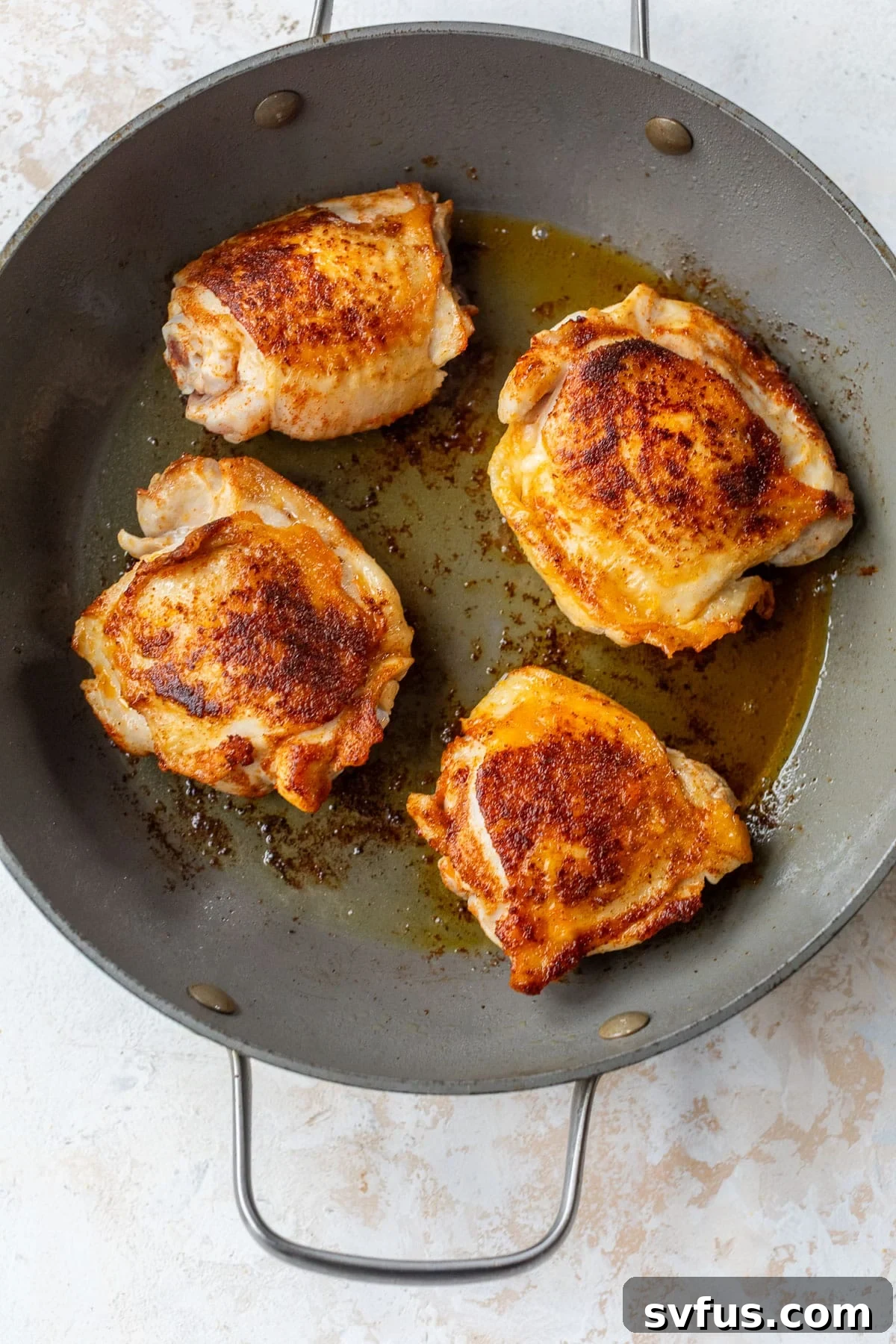 overhead view of seasoned chicken thighs being seared in a skillet.
