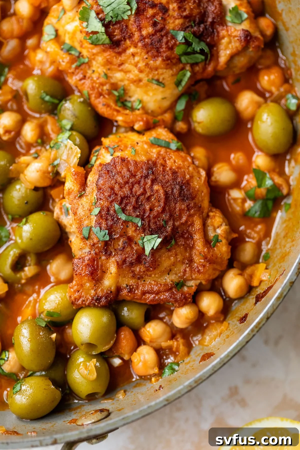 overhead view of Moroccan chicken thighs in a chickpea and olive sauce in a large pan.