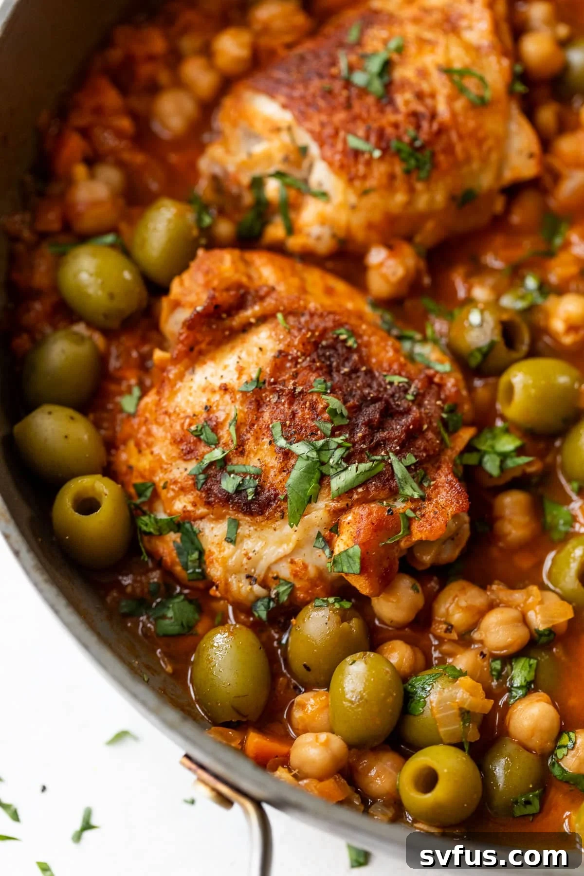 side view of Moroccan chicken thighs in a chickpea and olive sauce in a large pan.
